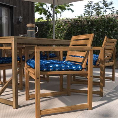 Terrassengarnitur mit rechteckigem Tisch, 4 Holzstühlen, blauen Kissen, Terrassengrün.
