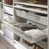 Weißer Netzkorb mit ordentlich gefalteten grauen Pullovern in einem Schrank.