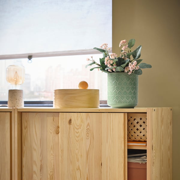 Holzschrank mit grüner Blumenvase und einer runden Holzkiste.