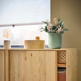 Holzschrank mit grüner Blumenvase und einer runden Holzkiste.