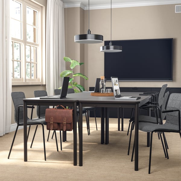 Moderner Konferenzraum mit schwarzen Stühlen um einen großen Tisch in der Nähe eines Fensters mit Vorhängen, Fernseher an dunkler Wand.