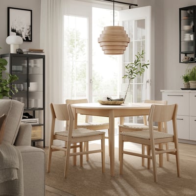 Moderner Essbereich mit rundem LÄTTBETONG-Teppich, hellbraunen Stühlen, Holztisch, Hängelampe und großem Fenster.