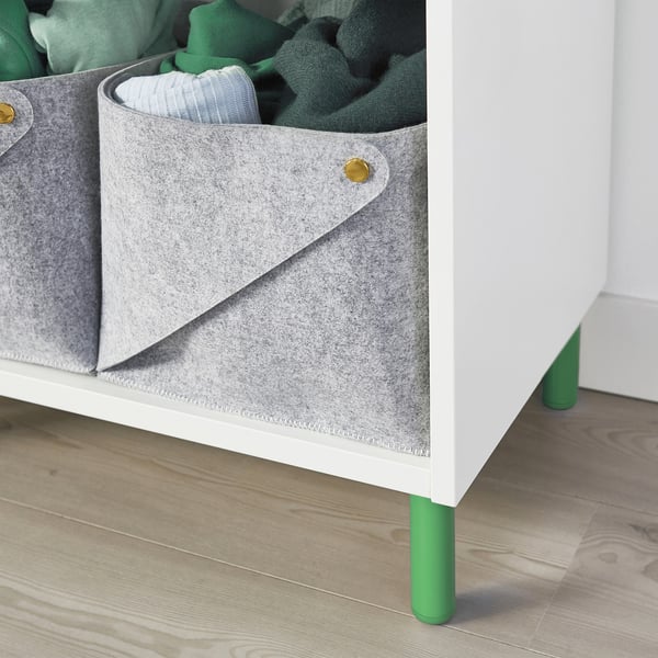 Weißer Stauraum mit grauem Stoffbehälter und grünen Beinen auf Holzboden.