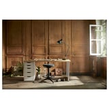 Kompaktes Home-Office-Setup: weißer LAGKAPTEN-Schreibtisch mit Schubladenschrank, schwarzem Drehstuhl und verstellbarer Lampe an einer Holzpaneelwand mit Fenster.