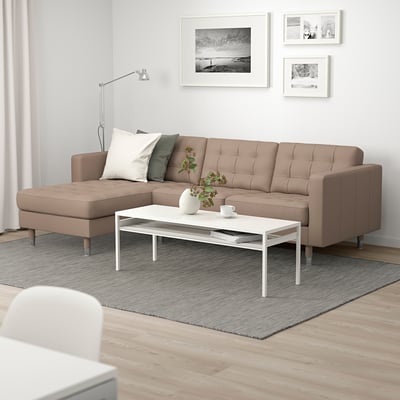 Modernes Wohnzimmer mit hellbraunem L-förmigem Sofa, weißem Couchtisch, grauem Teppich und Stehlampe.