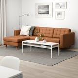Modernes Wohnzimmer mit großem braunem Ledersofa, weißem Couchtisch, grauem Teppich und Wandkunst. Helle und gemütliche Einrichtung.