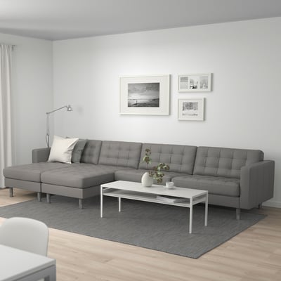Modernes Wohnzimmer mit großem grauem LANDSKRONA-Sofa, weißem Couchtisch und Wandkunst. Das Sofa ist im Vergleich zu Tisch und Teppich riesig.