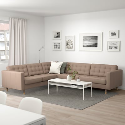 Modernes Wohnzimmer mit großem beigem L-förmigen Sofa, weißem Couchtisch, grauem Teppich und Wandkunst; Helles und gemütliches Dekor.