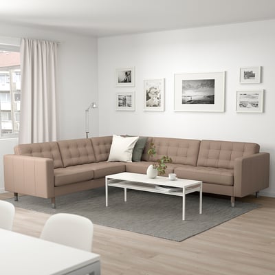 Modernes Wohnzimmer mit beigem L-förmigem Sofa, weißem Couchtisch, grauem Teppich, Stehlampe und schwarz/weißer Wandkunst.