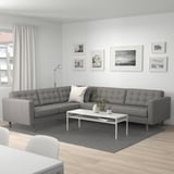 Modernes Wohnzimmer mit grauem LANDSKRONA-Sofa, Teppich, weißem Couchtisch, Schwarz-Weiß-Fotogalerie, Lampe und durchsichtigen Vorhängen.