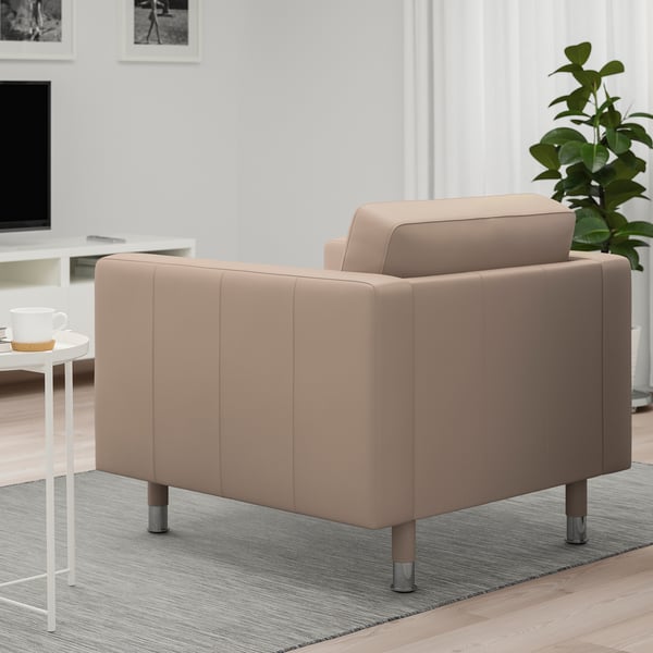 Ein moderner hellbrauner Sessel mit Metallbeinen steht auf einem Teppich in einem Wohnzimmer, daneben steht ein Couchtisch mit einer Tasse.