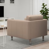 Ein moderner hellbrauner Sessel mit Metallbeinen steht auf einem Teppich in einem Wohnzimmer, daneben steht ein Couchtisch mit einer Tasse.