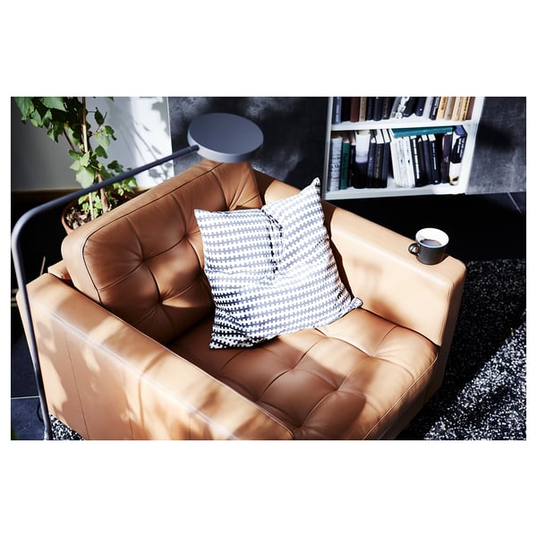 Modernes Wohnzimmer mit hellbraunem Ledersessel, geometrischem Kissen, Becher, Pflanze und Bücherregal.