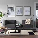 Minimalistisches Wohnzimmer mit dunkelgrauem LILLEHEM-Sofa, Schwarz-Weiß-Kunst, gemustertem Teppich und grüner Tasse auf kleinem Tisch.