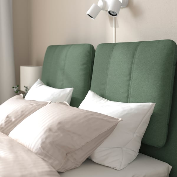 Ein grünes, schräges Kopfteil-Schlafsofa mit mehreren Kissen und einer weißen Lampe darüber.