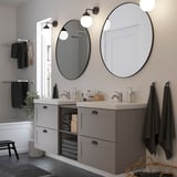Modernes Badezimmer mit großen runden Lindby-Spiegeln, dunklen Rahmen, Waschtisch und Wandleuchten. Dekoriert mit Handtüchern, Pflanzen und Körben.