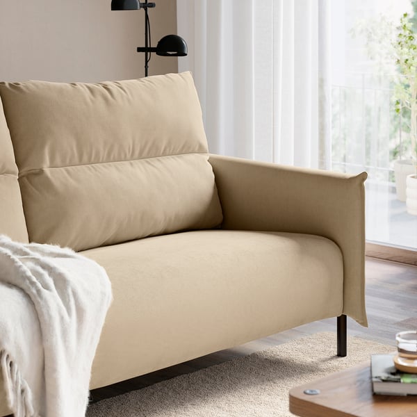 Sofa in neutraler Farbe mit Kissen, hoher Rückenlehne und schwarzen Beinen am Fenster.