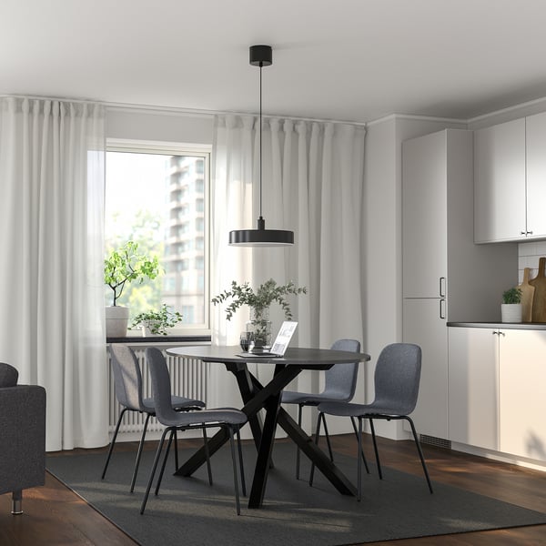 Modernes Esszimmer mit rundem Tisch, grauen Stühlen, Pendelleuchte, weißen Vorhängen, minimalistischer Küche.