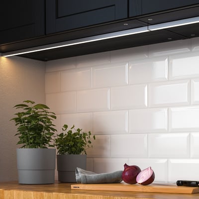 Küche mit LED-Leuchten unter dem Schrank, die die Arbeitsplatte beleuchten. Pflanzen und Zwiebeln auf der Holztheke.