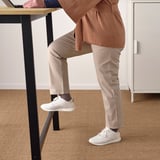 Person, die auf der Fußstütze neben dem Stehtisch steht und am Laptop arbeitet.