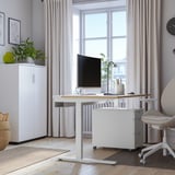 Modernes Homeoffice mit verstellbarem MITTZON-Schreibtisch, Monitor, Stuhl, Schrank, Pflanzen und Fenster.