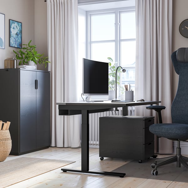 Modernes Home-Office-Setup mit höhenverstellbarem MITTZON Schreibtisch, grauem Stuhl, Computer, Lampe und Aufbewahrungsschrank. Großes Fenster mit Vorhängen.