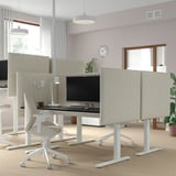 MITTZON Sitz-Steh-Schreibtische mit hellbeigen Bildschirmen, Doppelmotoren, in modernem Büro mit Pflanzen, Licht und Uhr.
