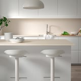 Zwei MÖCKLARP Hocker unter der Kücheninsel mit Tellern, Besteck und Kuppellampe.