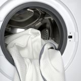 Waschmaschine mit weißer Bettwäsche, einschließlich einer Matratzenauflage, was auf Pflege- und Reinigungsfreundlichkeit hinweist.