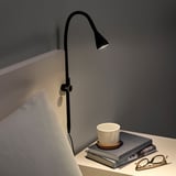 Schwarze verstellbare Klemmlampe am Bett, die einen Stapel Bücher mit einer Tasse darauf beleuchtet.