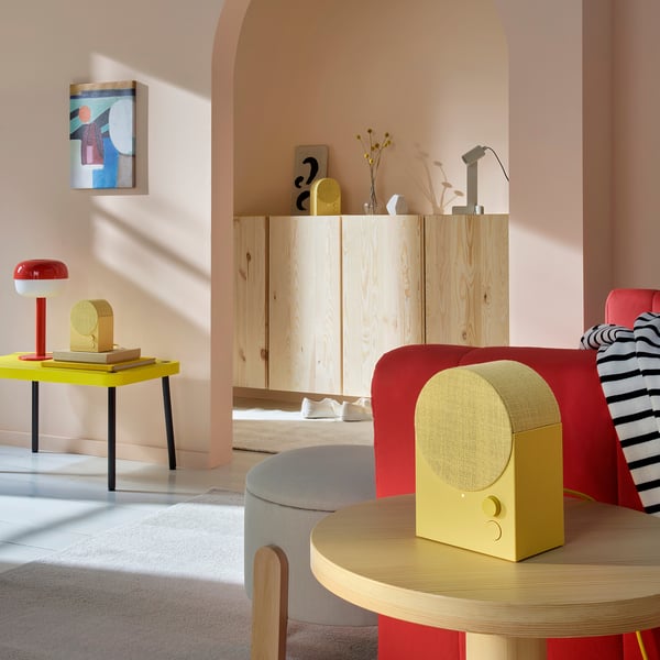 Modernes Wohnzimmer mit gelbem Lautsprecher, rotem Sofa, grauem Kissen und roter Lampe.