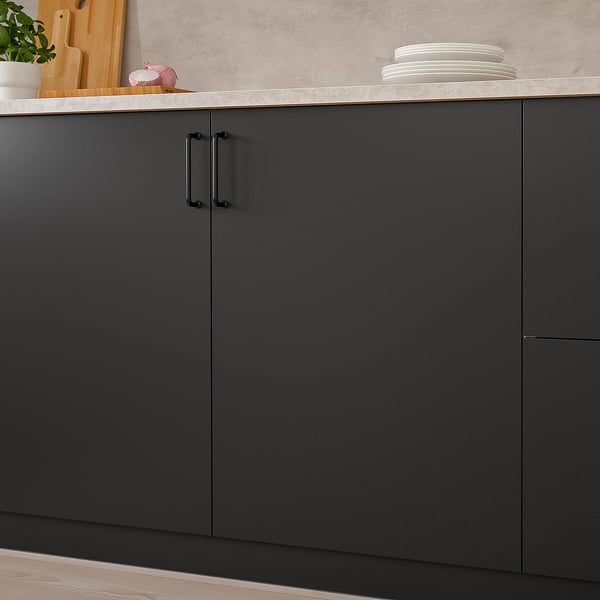 Moderne Küche mit dunkelgrauen Schränken. Schwarze Griffe, ein Stapel Teller, Holzbrett und Dekorationsgegenstände auf der Arbeitsplatte.