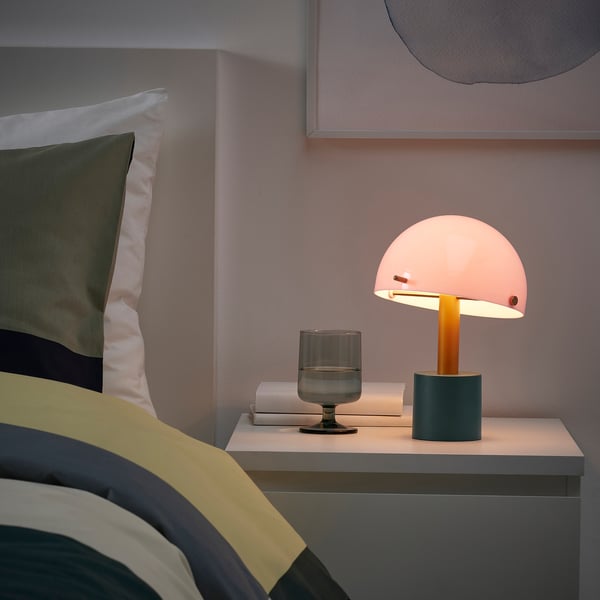 Orangefarbene NÖDMAST Lampe auf Nachttisch mit Büchern und Glas, die ein gemütliches Licht wirft.