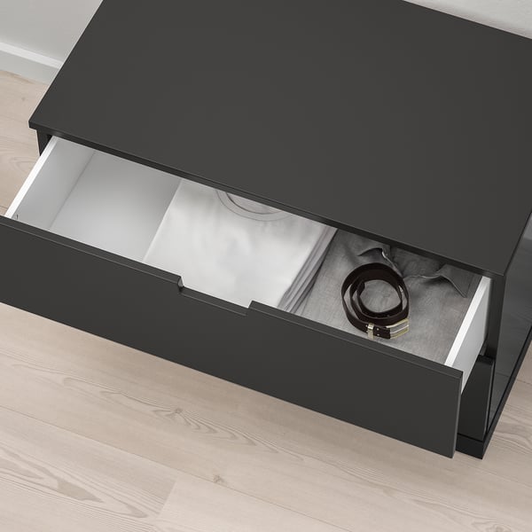 Die schwarze NORDLI-Kommode lässt sich öffnen und gibt den Blick auf die ordentlich gefaltete Kleidung und einen Gürtel frei, der ihre Aufbewahrungsfähigkeit demonstriert.