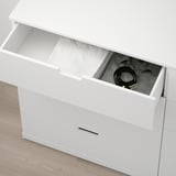 Weiße NORDLI-Kommode mit offener Schublade, die den Blick auf gerollte Gegenstände und Kabel freigibt und die Aufbewahrungsfunktionalität und den integrierten Sicherheitsbeschlag zeigt.