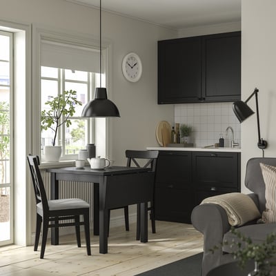 Moderne schwarze Essgarnitur mit klappbarem Blatttisch und Stühlen. Großes Fenster, leuchtendes Grün und eine elegante schwarze Küche.