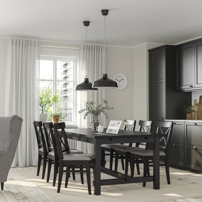 Nordvik Esszimmergarnitur mit ausziehbarem Tisch und gepolsterten Stühlen, bis zu 8 Sitzplätzen, in einem gemütlichen Raum mit dunklen Schränken und weißen Vorhängen.