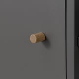 Ein schlanker, moderner Schrankgriff aus zylindrischem Holz. Auf einer glatten, grauen Oberfläche, die ihre natürliche, strukturierte Ausstrahlung unterstreicht.