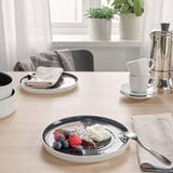 Ein Tisch mit OMBONAD-Keramiktellern, auf dem ein Dessert mit Beeren und Sahne präsentiert wird, bereit zum Essen.