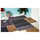 Verschiedene Fußmatten, die im Innenbereich ausgestellt sind, jede mit unterschiedlichen Designs und Farben, platziert auf hellen Holzböden neben weißen Möbeln und einer blauen Wand.