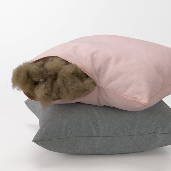 Stapel von zwei Kissen, von denen eines offen ist und braune Füllstoffe und weiche, recycelte Materialien zeigt.
