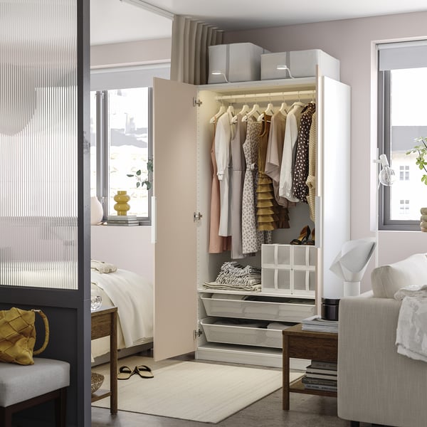 Geschlossener Kleiderschrank mit Kleidung, Regalen und Schubladen in einem gut organisierten Raum mit Bett und Stuhl.