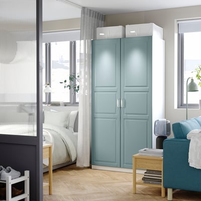 Modernes Schlafzimmer mit blau-grünem PAX-Kleiderschrank mit organisiertem Stauraum, glatten Türen und weißen Boxen, die das minimalistische Dekor aufwerten.