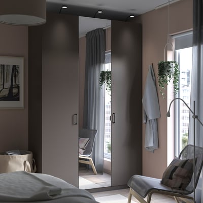 Modernes Schlafzimmer mit grauem PAX-Kleiderschrank mit Spiegeltüren, elegantem Design mit hängenden Pflanzen und einem gemütlichen weißen Stuhl am Fenster.