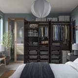 Modernes Schlafzimmer mit blauen Wänden, schwarzem PAX-Kleiderschrank, Kleidung und sanfter Beleuchtung.