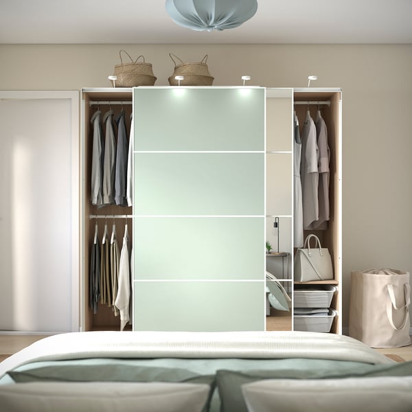 Schlafzimmer mit offenem Kleiderschrank mit Kleidung, einer Handtasche und Aufbewahrungskörben obendrauf. Schiebetüren geben den Blick auf hängende Kleidungsstücke und innere Organizer frei.