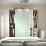 Schlafzimmer mit offenem Kleiderschrank mit Kleidung, einer Handtasche und Aufbewahrungskörben obendrauf. Schiebetüren geben den Blick auf hängende Kleidungsstücke und innere Organizer frei.