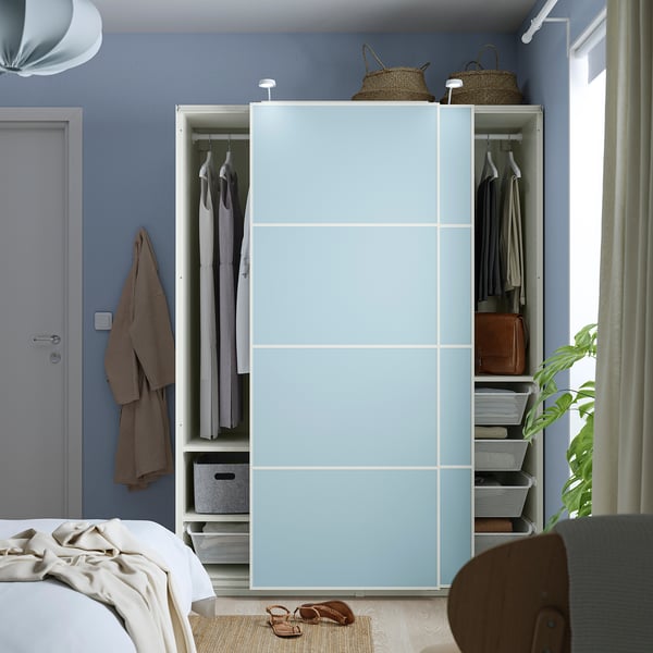 Hellblauer Kleiderschrank mit Schiebetüren, hängender Kleidung, Regalen und Körben, in der Nähe eines Bettes positioniert.