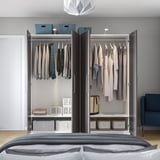 Offener Kleiderschrank mit Kleidung, Körben, Schubladen im Schlafzimmer mit Bett.