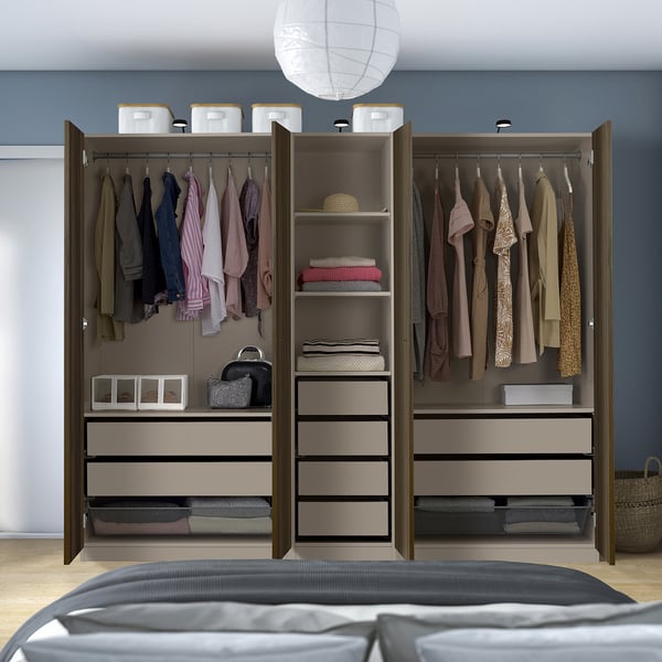 Moderner offener Kleiderschrank mit Kleiderbügeln, Regalen, Behältern und Schubladen, in denen Kleidung und Accessoires ordentlich vor blauer Wand organisiert sind.